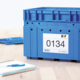 Blaue Kunststoffbox mit der Aufschrift "0134" und einem Etikett. Im Hintergrund ein Notizblock und ein Stift.