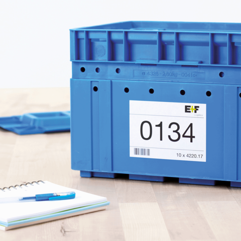 Blaue Kunststoffbox mit der Aufschrift "0134" und einem Etikett. Im Hintergrund ein Notizblock und ein Stift.