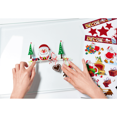 Hände arrangieren Weihnachtsdekorationen, darunter ein Weihnachtsmann, Tannenbäume und ein Herz, auf einer glatten Oberfläche.