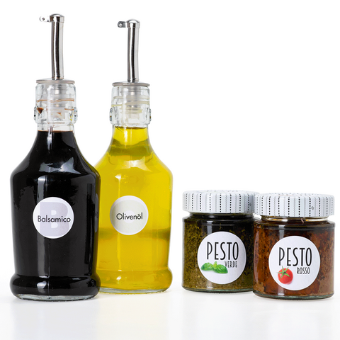 Deux bouteilles de balsamique et d'huile d'olive ainsi que deux pots de pesto de différentes variétés sur un fond blanc.