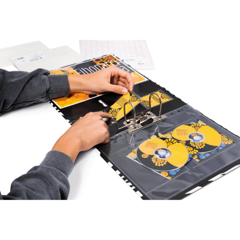 Eine Person öffnet einen Ordner mit CD-Hüllen, die gelbe CDs enthalten, während ein Kalender und Dokumente im Hintergrund sichtbar sind.