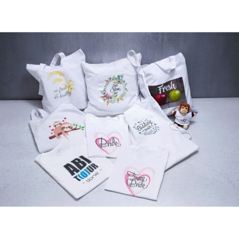 Verschiedene weiße Taschen und Kissen mit bunten Aufdrucken, darunter "Bride" und "Fresh", sowie ein kleines Stofftier.