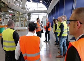 Un groupe de personnes en gilets de sécurité écoute un intervenant dans un environnement industriel.