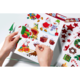 Hände halten ein Blatt mit bunten Weihnachtsstickern, darunter Weihnachtsmann, Geschenke, Schneemann und Weihnachtsbaum.