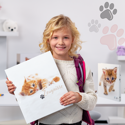 Un fille aux boucles blondes tient un classeur avec une image de chat. En arrière-plan, on peut voir d'autres classeurs et des jouets.