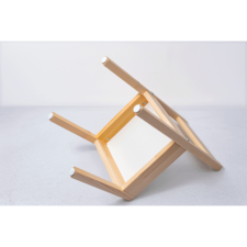 Umgedrehter Holzstuhl mit sichtbaren Beinen und einer weißen Sitzfläche auf einem grauen Untergrund.