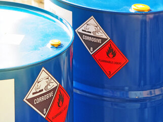 Deux fûts bleus avec des étiquettes d'avertissement pour des liquides corrosifs et inflammables.