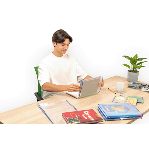 Ein junger Mann sitzt an einem Tisch, nutzt ein Tablet und hat mehrere Bücher sowie Schreibmaterialien vor sich. Eine Pflanze ist ebenfalls sichtbar.