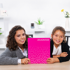 Deux filles sont assises à une table et tiennent un cahier rose avec l'inscription "TÉMOIGNAGES". Elles sourient à la caméra.