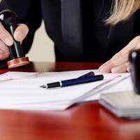 Une main tamponne des documents sur une table, tandis qu'une autre main tient un stylo.