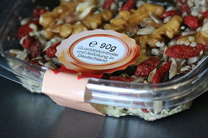 Un bol transparent contenant un mélange de noix, de graines et de fruits secs, étiqueté avec des informations nutritionnelles.
