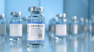 Flacon de vaccin COVID-19 avec une étiquette contenant des informations importantes telles que le numéro de lot et la date d'expiration, devant d'autres flacons flous.