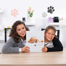 Une femme et une fille tiennent un livre avec une couverture de chaton, assises à une table. En arrière-plan, des éléments décoratifs sont visibles.