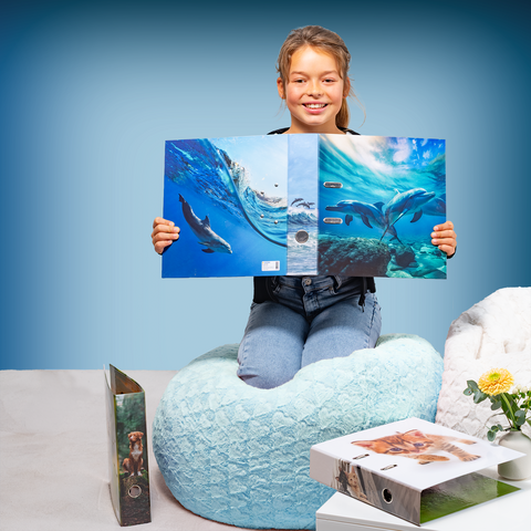 Un fille est assise sur un pouf et tient un livre avec des images de dauphins. À côté d'elle, d'autres livres sont posés sur une table.