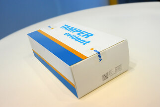 Emballage avec l'inscription "TAMPER evident" en bleu et orange, fabriqué par HERMA.