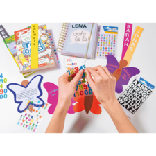 Hände platzieren bunte Aufkleber auf Schmetterlingen und Karten, um eine kreative Bastelaktivität zu zeigen. Bücher und ein Notizbuch sind ebenfalls sichtbar.