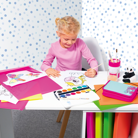Un petit garçon est assis à une table, peignant à l'aquarelle, entouré de papier coloré et de dessins.