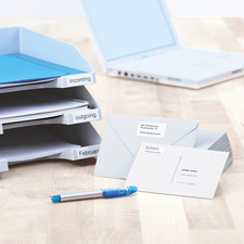 Classeur avec des compartiments étiquetés pour les documents entrants et sortants, à côté des enveloppes et un stylo bleu sur une table.