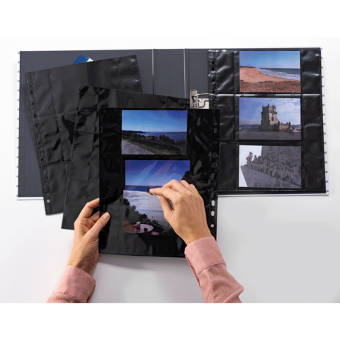 Eine Person blättert durch eine Fotohülle mit mehreren Bildern, während ein Fotoalbum im Hintergrund sichtbar ist.