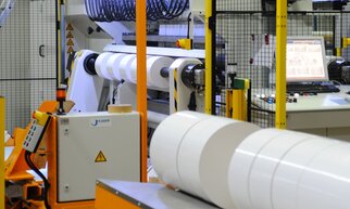 Machines industrielles pour le traitement de matériaux en rouleaux, avec un panneau de contrôle en arrière-plan et une clôture de sécurité.