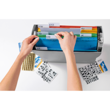 Hände sortieren farbige Ordner in einer Aufbewahrungsbox mit beschrifteten Trennblättern. Auf dem Tisch liegen zusätzliche Etiketten.