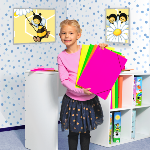Ein Mädchen mit lockigem Haar hält bunte Bastelpapiere in der Hand. Im Hintergrund sind Bilder von Bienen und einer Blume an der Wand.