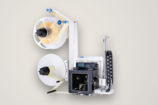 Un appareil avec deux bobines, un mécanisme de pression et divers éléments de contrôle, utilisé pour le traitement du papier ou des étiquettes.