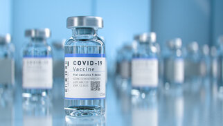 Flacons de vaccin contre la COVID-19 sur une table, contenant un liquide clair et une étiquette avec des informations importantes.
