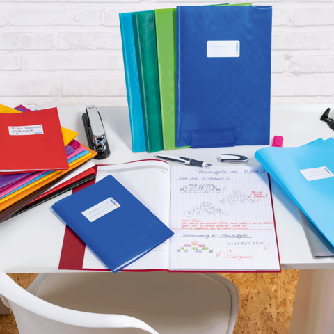 Des classeurs colorés et des cahiers sur une table, à côté d'une agrafeuse et de fournitures d'écriture.