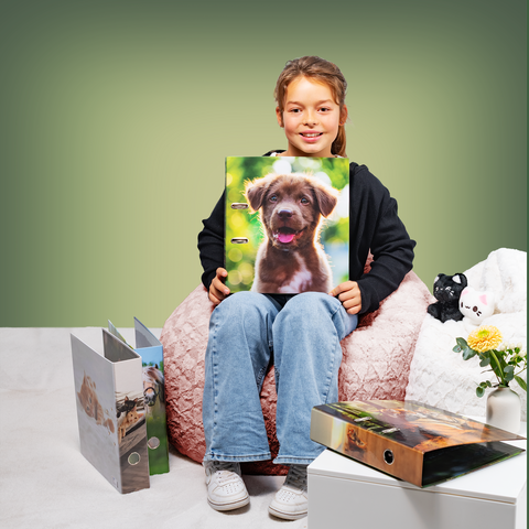 Un fille est assise sur un pouf et tient un dossier avec une photo de chien. À côté d'elle, il y a d'autres dossiers et une petite plante.