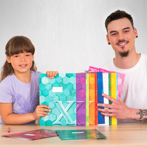 Ein Kind und ein Mann halten bunte, geometrische Muster in der Hand. Auf dem Tisch liegen weitere Muster und ein großes, farbiges Heft.