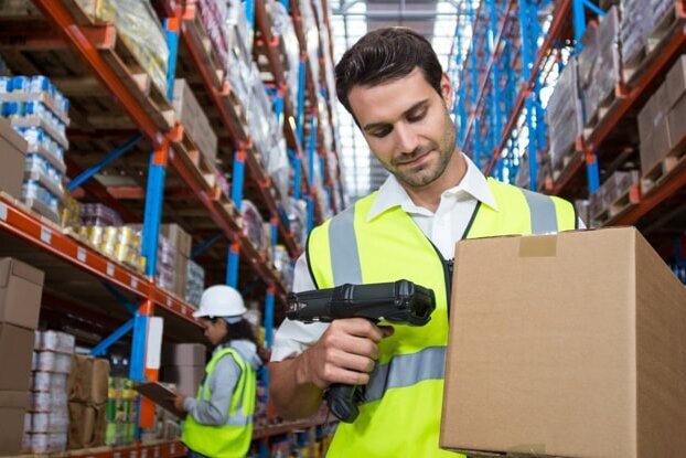 Employé logistique en train de scanner une étiquette d'expédition sur un carton, dans l'entrepôt, format paysage.
