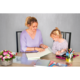 Eine Frau und ein Kind sitzen an einem Tisch und betrachten gemeinsam ein Buch. Auf dem Tisch liegen verschiedene Schreibmaterialien und Blumen.