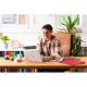 Ein junger Mann sitzt an einem Schreibtisch mit einem Laptop, umgeben von Schreibmaterialien und Pflanzen, und arbeitet konzentriert.