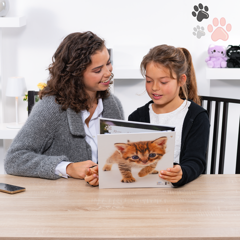 Une femme et une fille sont assises à une table et regardent ensemble un livre illustré de chats.