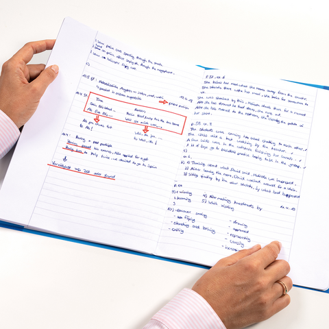 Une personne tient un carnet ouvert avec des notes manuscrites et des surlignages. Les pages contiennent des informations sur divers sujets.