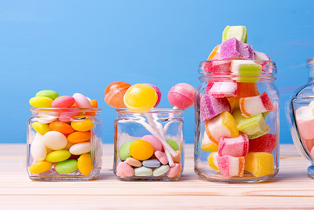 Des bonbons colorés dans différents bocaux sur un fond en bois, avec un arrière-plan bleu.