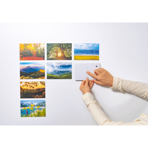 Eine Hand platziert eine kleine Notiz oder Karte an einer Wand, umgeben von mehreren Landschaftsbildern in einem Raster.