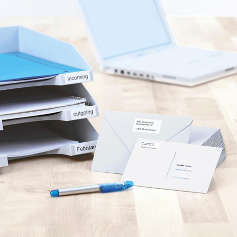 Ordner mit Beschriftungen für eingehende und ausgehende Dokumente, Umschläge mit Adressen und ein blauer Stift auf einem Tisch.