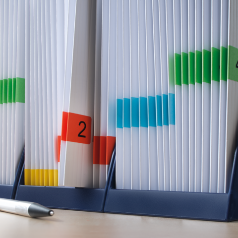 Classeur avec des étiquettes colorées et des documents marqués dans un support, à côté un stylo.