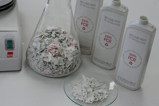 Un erlenmeyer avec du matériau broyé et trois bouteilles contenant 100 % de matériau recyclé pour PCR, sur une table.