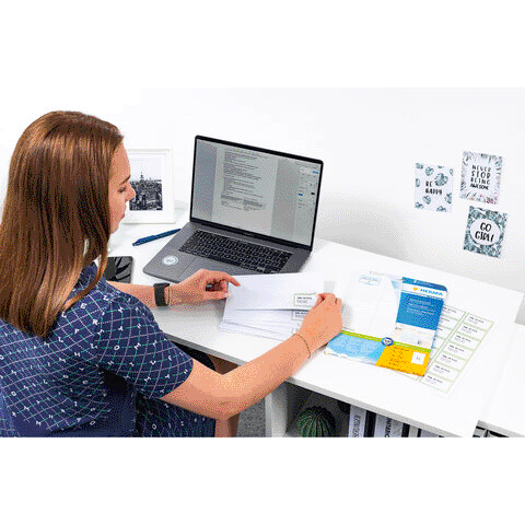 Eine Person sitzt an einem Schreibtisch, arbeitet am Laptop und sortiert Dokumente. Auf dem Tisch liegen verschiedene Papiere und Unterlagen.