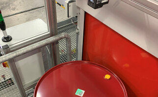 Conteneur rouge avec une étiquette et un couvercle jaune, placé dans un environnement industriel avec des machines en arrière-plan.