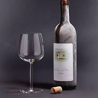 Une bouteille de vin avec une étiquette et un verre à côté, posée sur un fond sombre. Un bouchon est tombé par terre.