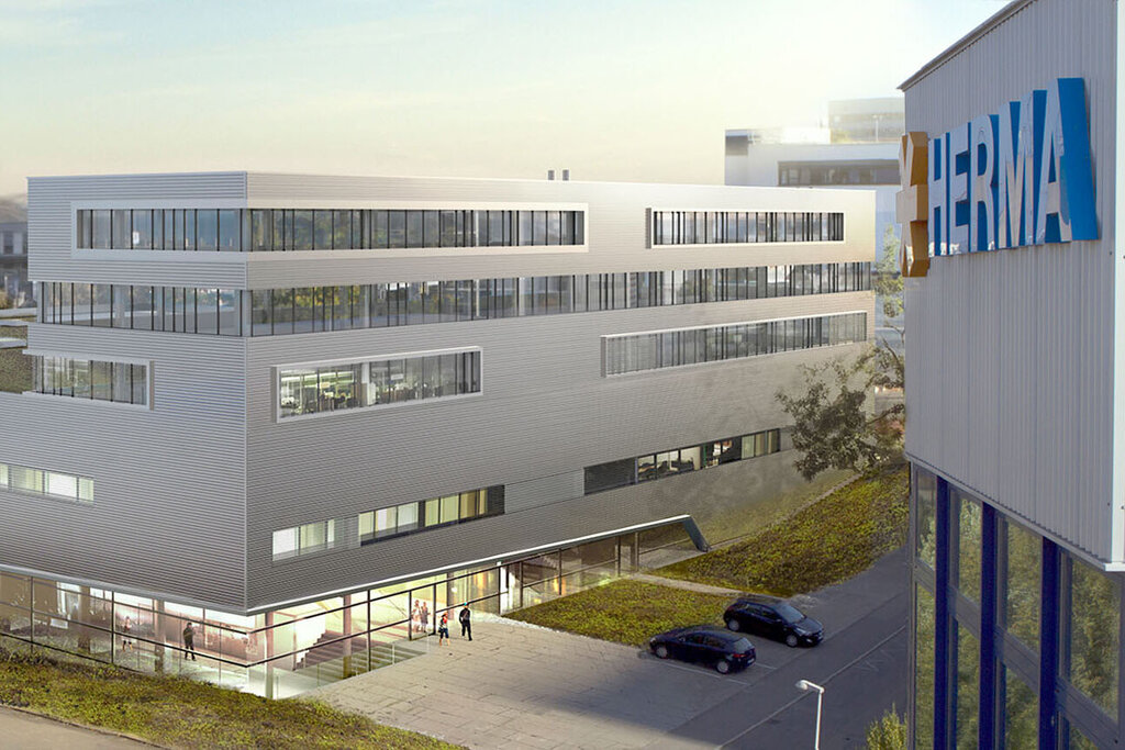 Bâtiments de bureaux modernes avec des toits plats et de grandes fenêtres, entourés d'un espace vert et d'un parking.