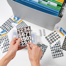 Eine Person hält ein Blatt mit bunten Aufklebern über einem geöffneten Planer, während sie Notizen macht.