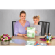 Eine Frau und ein Mädchen sitzen an einem Tisch und halten ein grünes Heft. Auf dem Tisch liegen Schreibmaterialien und Blumen.