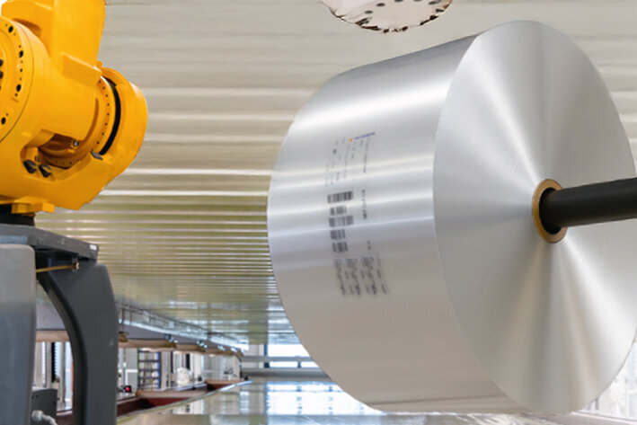 Un bras robotisé industriel jaune monte un grand composant argenté dans un environnement de fabrication moderne.