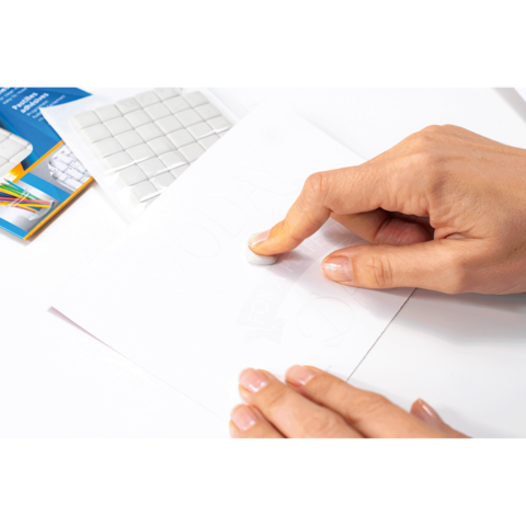 Eine Hand verwendet einen Radiergummi, um Bleistiftmarkierungen auf einem Blatt Papier zu entfernen. Im Hintergrund sind Bastelmaterialien sichtbar.