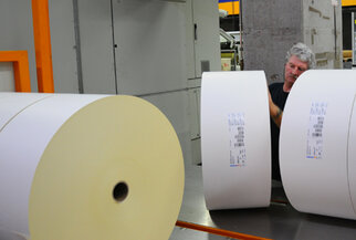 Un ouvrier dans une imprimerie vérifie de grands rouleaux de papier tout en se tenant à une machine.